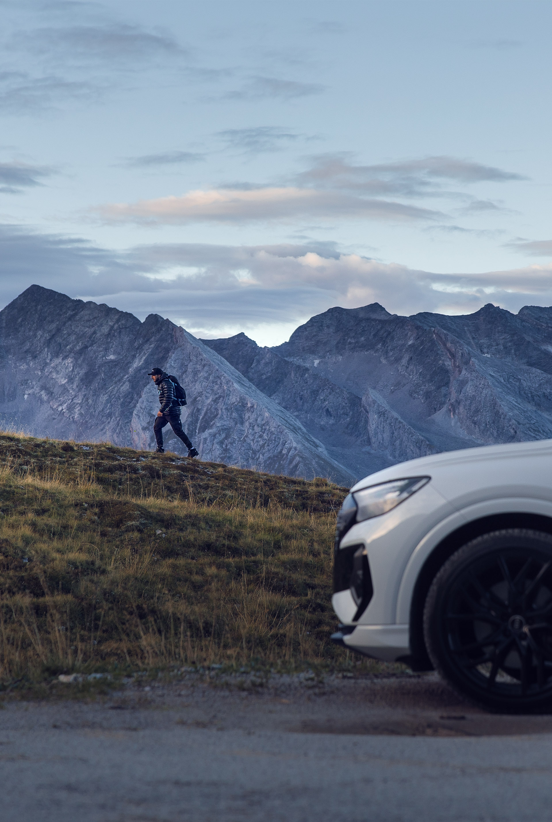 Der weiße Audi Q4 e-tron steht vor einem Berg, wo Tom Klocker zu Fuß hochwandert.